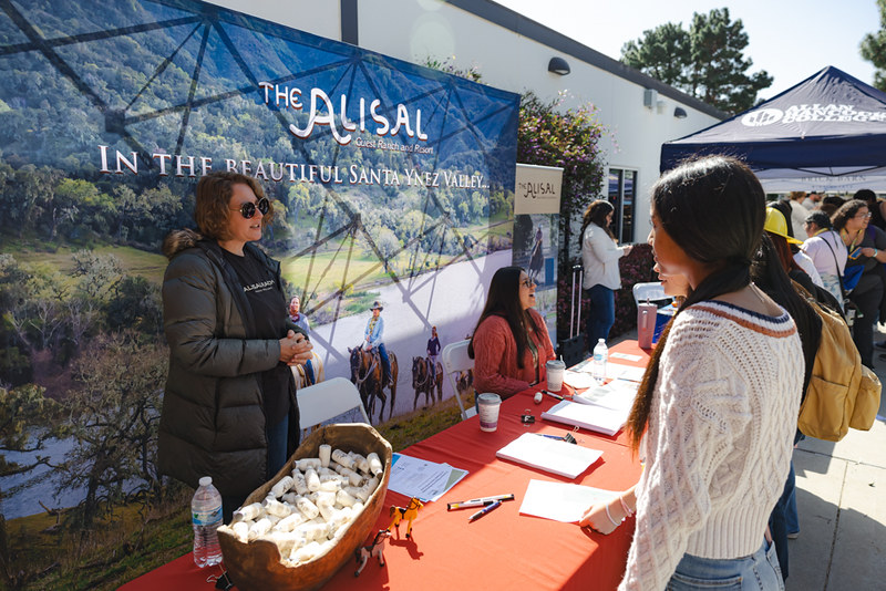 A woman at a table for Alisal Ranch speaks with a Hancock student. 