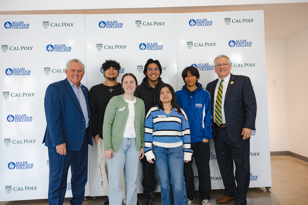 Cal Poly President Jeff Armstrong (far right) and Allan Hancock College Superintendent/President Kevin G. Walthers (far left) stand with a group of five Allan Hancock College students in front of a backdrop featuring the Cal Poly and Allan Hancock College logos. The group smiles for the photo, representing a collaboration event between the two institutions.