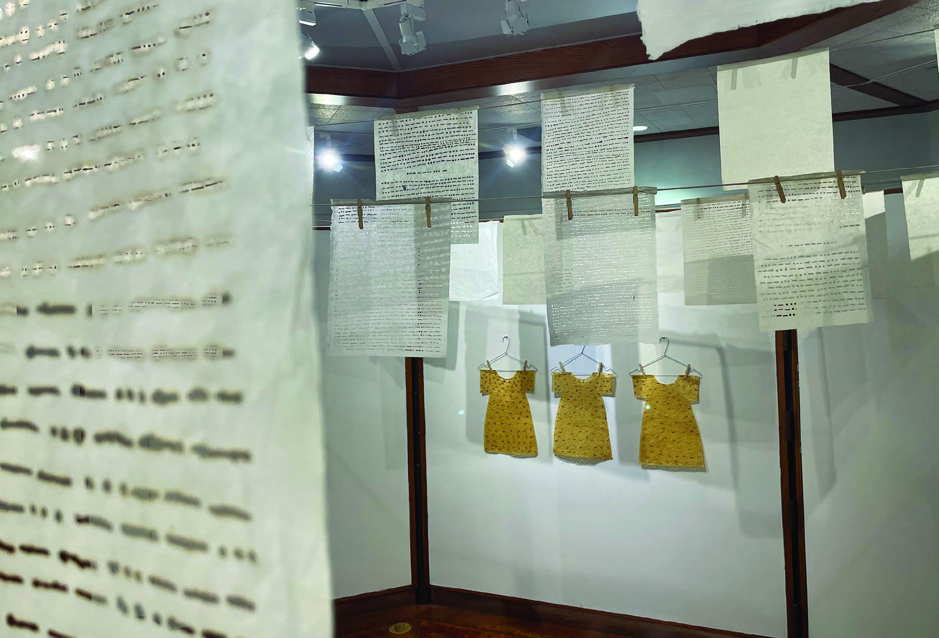 A t-shirt and several pieces of paper hang from the wall of an art gallery.