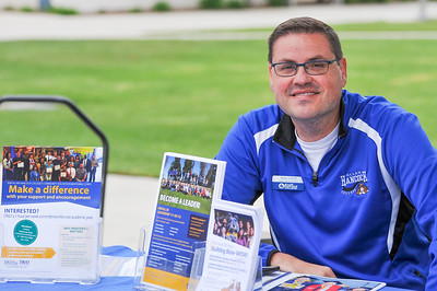 Outreach Staff member sits behind a table of promotional materials. 